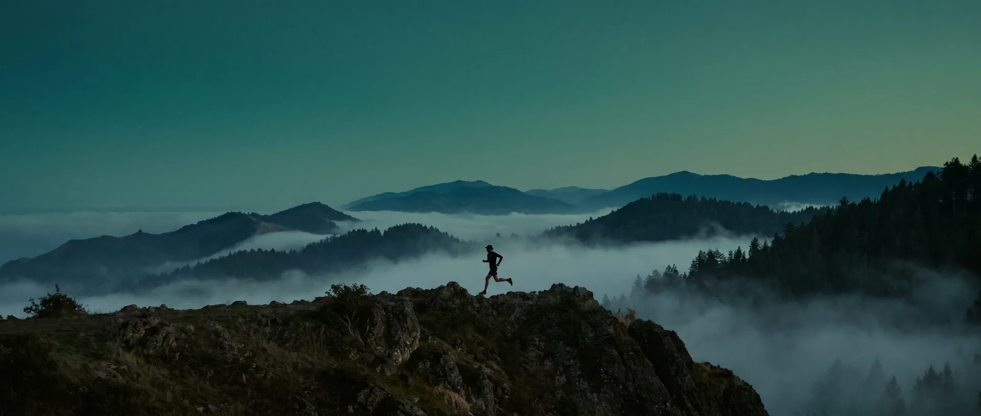 Trail runner silhouetted on a mountain ridge at dusk